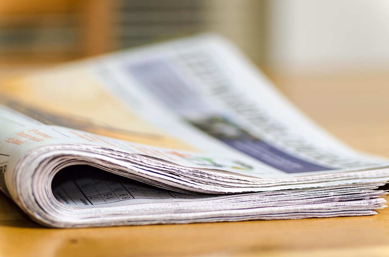 Lehdistötilaisuus mediatoimistossa, toimittajia ja sanomalehtiä ympärillä.