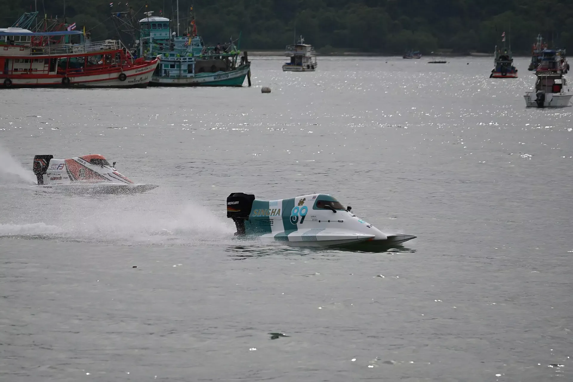 DFC 1324 Two sleek powerboats speed across a sun-sparkled harbor during a high-speed race leaving white spray in their wake as other vessels watch from the distance