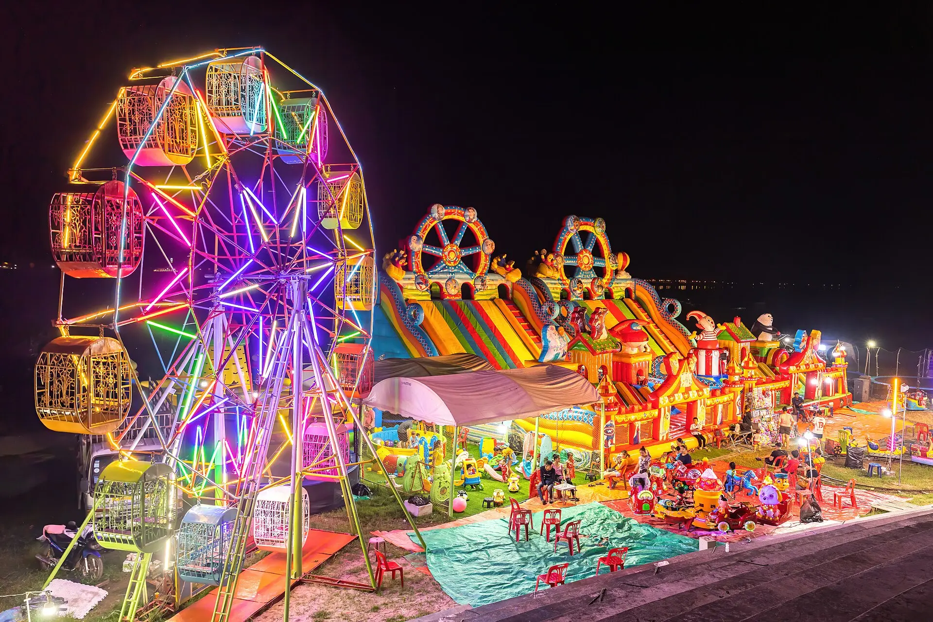 Illuminated Ferris wheel, bouncing castle and carousel at night in a funfair in Vientiane, Laos
